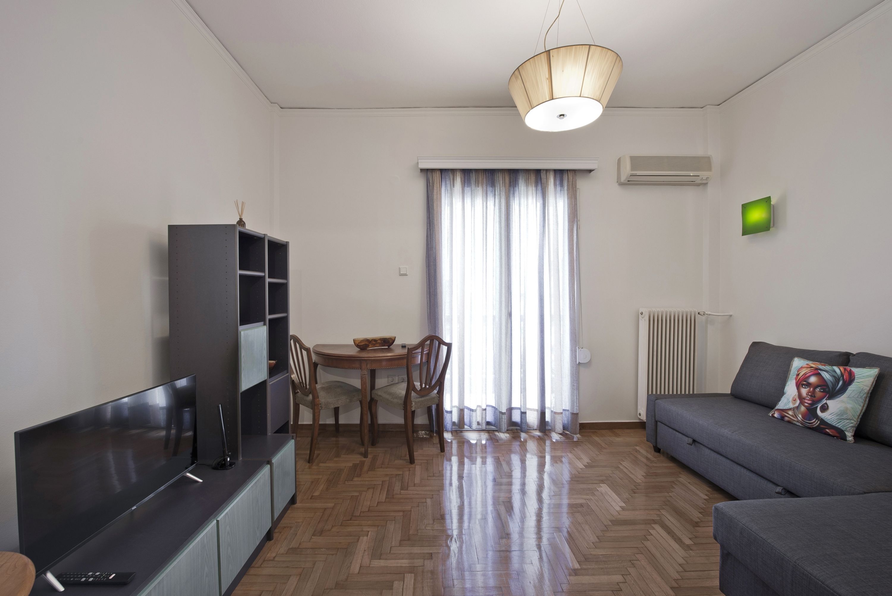 Ein modernes Wohnzimmer mit Flachbildfernseher, einer Couch, einem Esstisch mit Stühlen und einem Holzboden mit Fischgrätmuster.