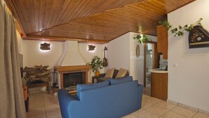 A cozy living room with a blue sofa, wooden ceiling, fireplace, and a kitchen area with a sink and countertop. - Apos Place in Pefki With 1 Bedrooms and 1 Bathrooms (Lykovrysi-Pefki)