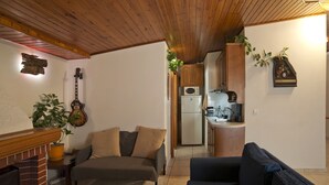 A cozy living room with a fireplace, a sofa, and a coffee table. A kitchen is visible in the background with wooden cabinets and a refrigerator. - Apos Place in Pefki With 1 Bedrooms and 1 Bathrooms (Lykovrysi-Pefki)