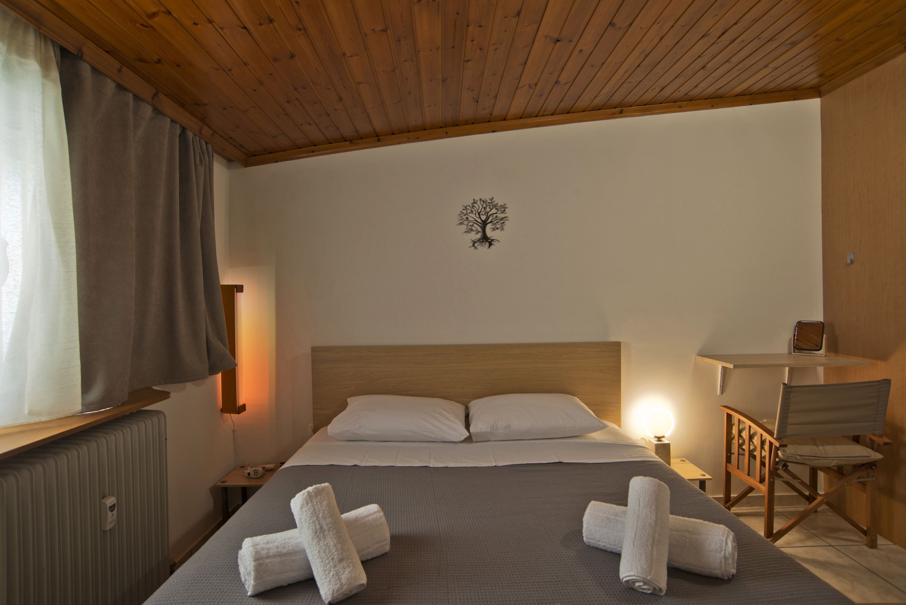 Un letto ben rifatto con due cuscini, una testiera in legno, un comodino con una lampada e un tavolino con una sedia.