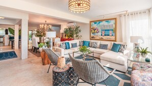 A modern living room with a white sofa, wicker chairs, a glass coffee table, and a chandelier. - Tenis Villa 18 in Casa De Campo (La Romana)
