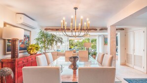 A dining area with a glass table, white chairs, a chandelier, and a red cabinet. - Tenis Villa 18 in Casa De Campo (La Romana)