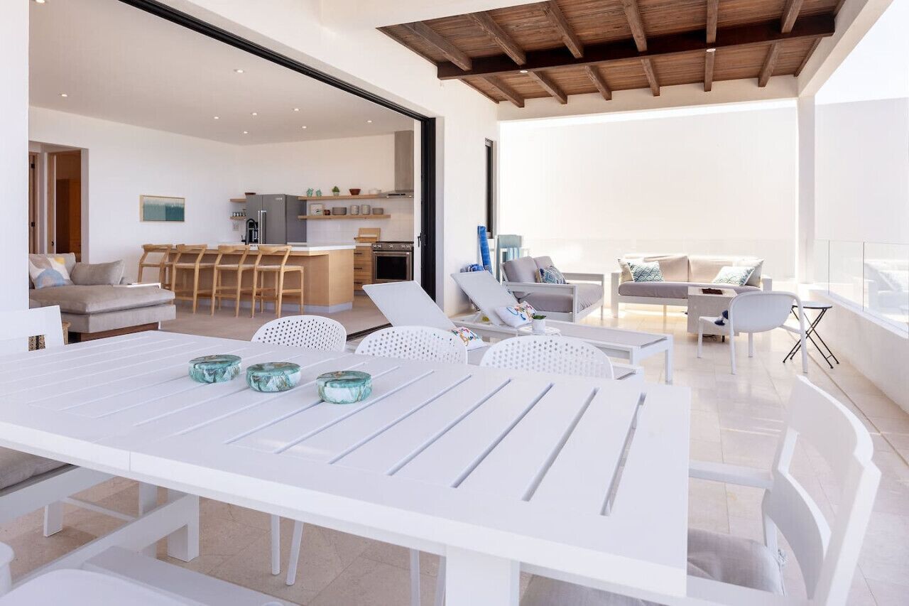 A modern, open-plan living area with a dining table, lounge chairs, and a kitchen in the background.