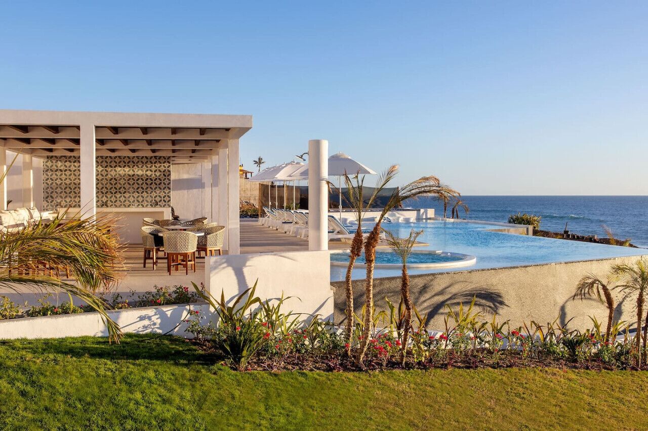 Ett semesterhotell med pool, solstolar och utsikt över havet.