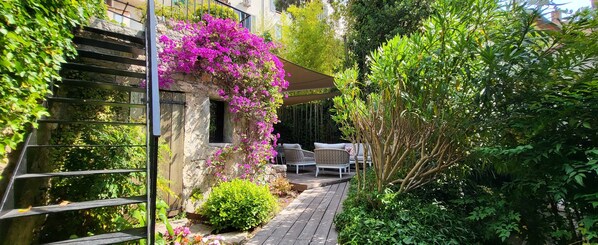 A stone building with a wooden deck, outdoor furniture, and lush greenery.