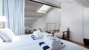 Et moderne hotelværelse med en pænt redt seng, en stol og udsigt til det fri gennem et ovenlys.
