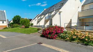 A residential building with a sloped roof, a front entrance, and a small garden with pink and yellow flowers. - Le P'tit Loup de Mer - Appt proche plage, terrasse (Saint-Nic)