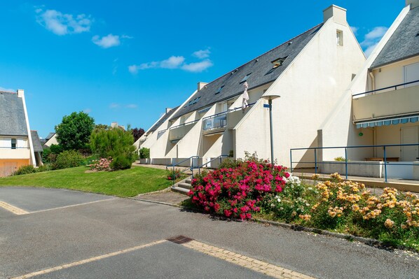 A residential building with a sloped roof, a front entrance, and a small garden with pink and yellow flowers. - Le P'tit Loup de Mer - Appt proche plage, terrasse (Saint-Nic)