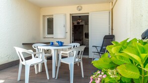A patio with a table and chairs, a door leading to an interior space, and a plant with green leaves and pink flowers. - Le P'tit Loup de Mer - Appt proche plage, terrasse (Saint-Nic)