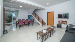 Un amplio salón con una mesa de comedor, sillas, un sofá, una escalera y un televisor montado en la pared.