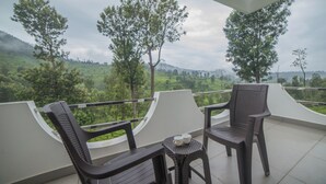 Un balcón con dos sillas y una mesita, con vista a un paisaje verde y exuberante con árboles y colinas.