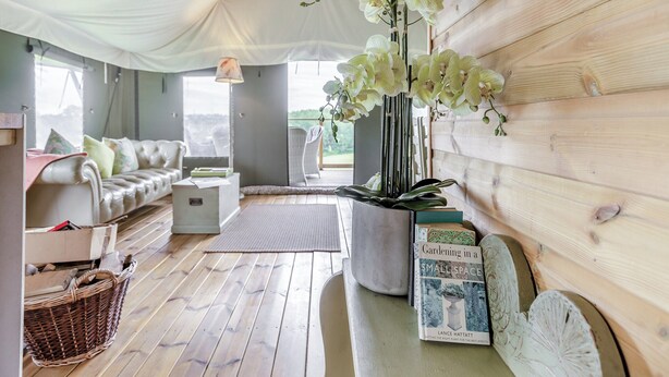 A cozy room with a white sofa, a small table, a book titled "Gardening in a Small Space," and a potted orchid plant. - Safari Tent Two - UK44405 (Ross-on-Wye)