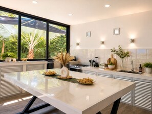 A modern kitchen with a large island, a view of greenery outside, and a clean, minimalist design.