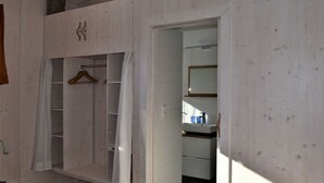 Een kamer met een houten garderobe, een kledingroede en een badkamer met spiegel en wastafel.