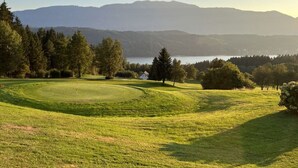Een golfbaan met een clubhuis, omringd door bomen en bergen op de achtergrond.