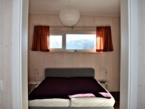 Et soveværelse med en seng, to sengeborde, et vindue med gardiner og en hængende lampe.