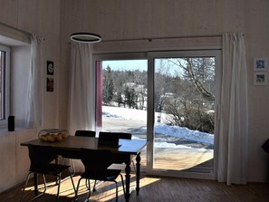 Et spiseområde med et bord og stole, udsigt til et sneklædt landskab gennem en glasdør, og en trægulv.
