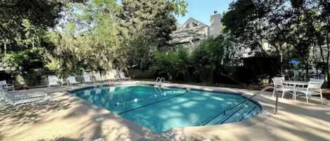 A swimming pool surrounded by lounge chairs and trees.