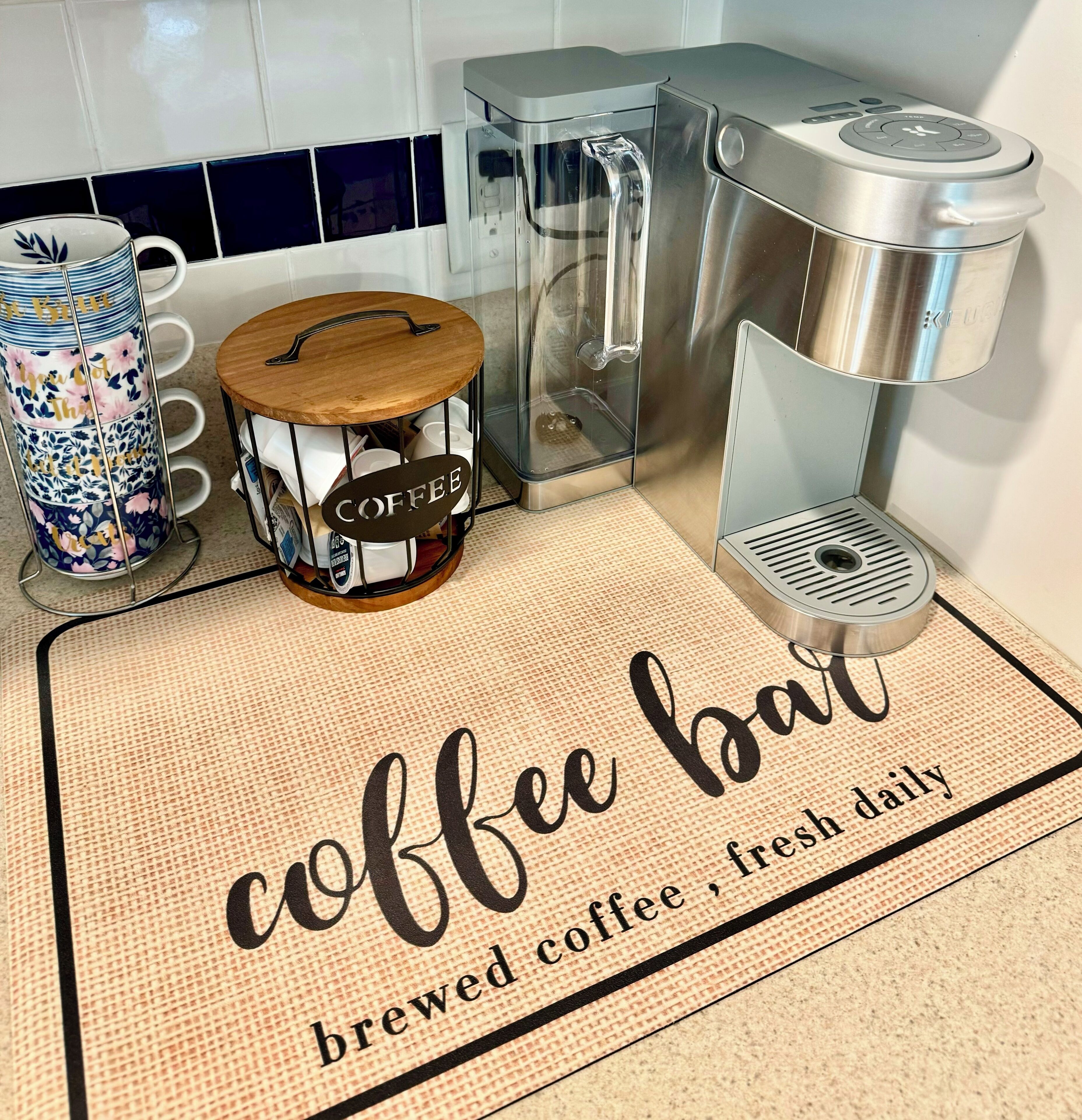 A kitchen with a coffee station, including a coffee maker, a coffee grinder, and a coffee-themed mat.