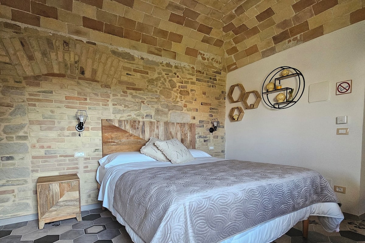 A bedroom with a brick ceiling, a bed with a patterned bedspread, hexagonal patterned flooring, and wall-mounted light fixtures.