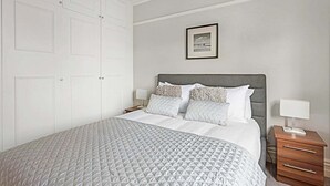 Quarto bem arrumado com uma cama grande, cabeceira cinza e um quadro na parede.