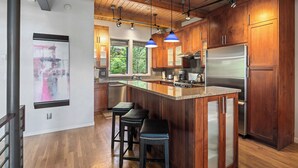 Une cuisine moderne avec des meubles en bois, un réfrigérateur en acier inoxydable et un coin bar avec des tabourets.
