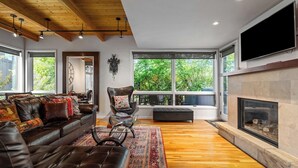Un salon moderne avec un canapé en cuir, une cheminée et de grandes fenêtres donnant sur un paysage verdoyant.