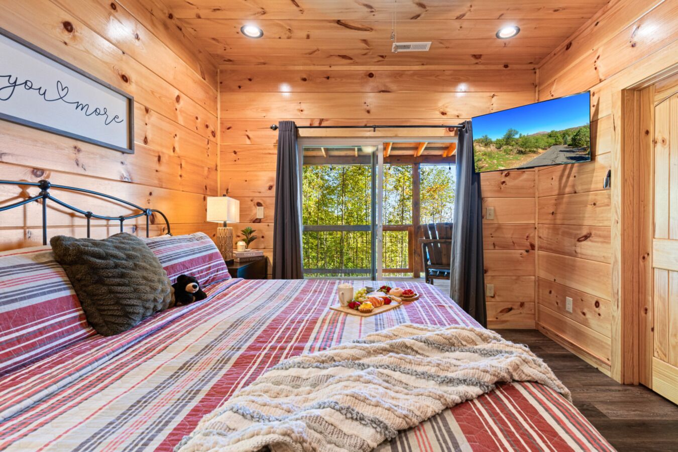 Une chambre confortable dans un chalet en bois, avec un lit, une table de chevet, une fenêtre donnant sur un beau paysage et un téléviseur fixé au mur.