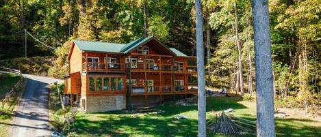 A two-story log cabin with a green roof, surrounded by a forest.