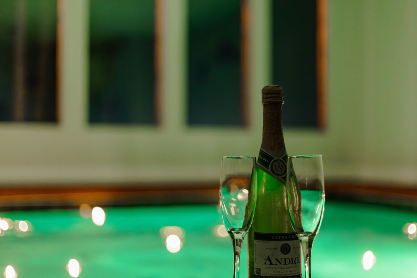 Una botella de vino Andre junto a dos copas sobre una mesa al lado de la piscina.