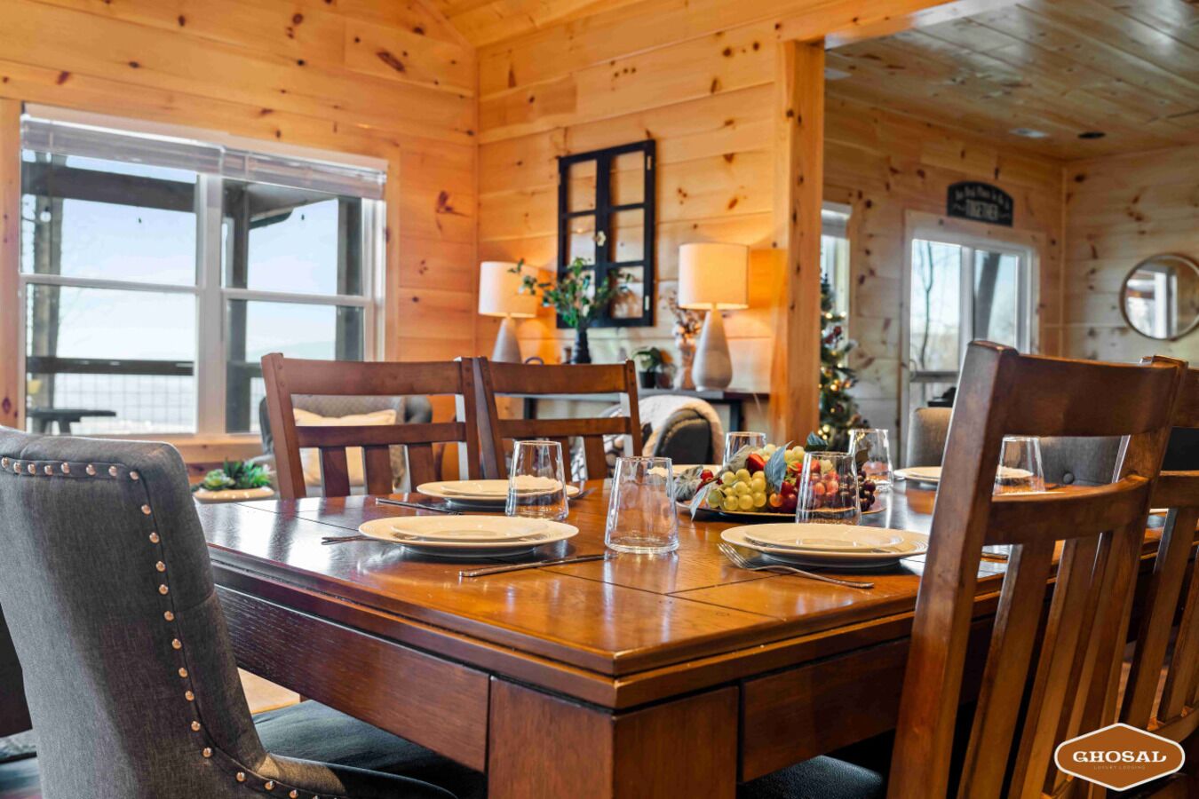 A wooden dining table set for four with chairs, a fruit platter, and a Christmas tree in the background.