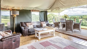 Een tent met een leren bank, een tafel, rieten stoelen en uitzicht op de omgeving.