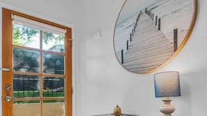 A wooden door with glass panels, a geometric-patterned cabinet, a round mirror with a beach scene, and a lamp on the cabinet.