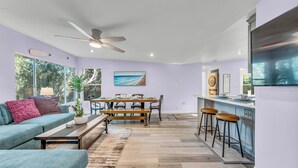 A modern living space with a dining area, a kitchen with a bar, and large windows offering a view of the outdoors.
