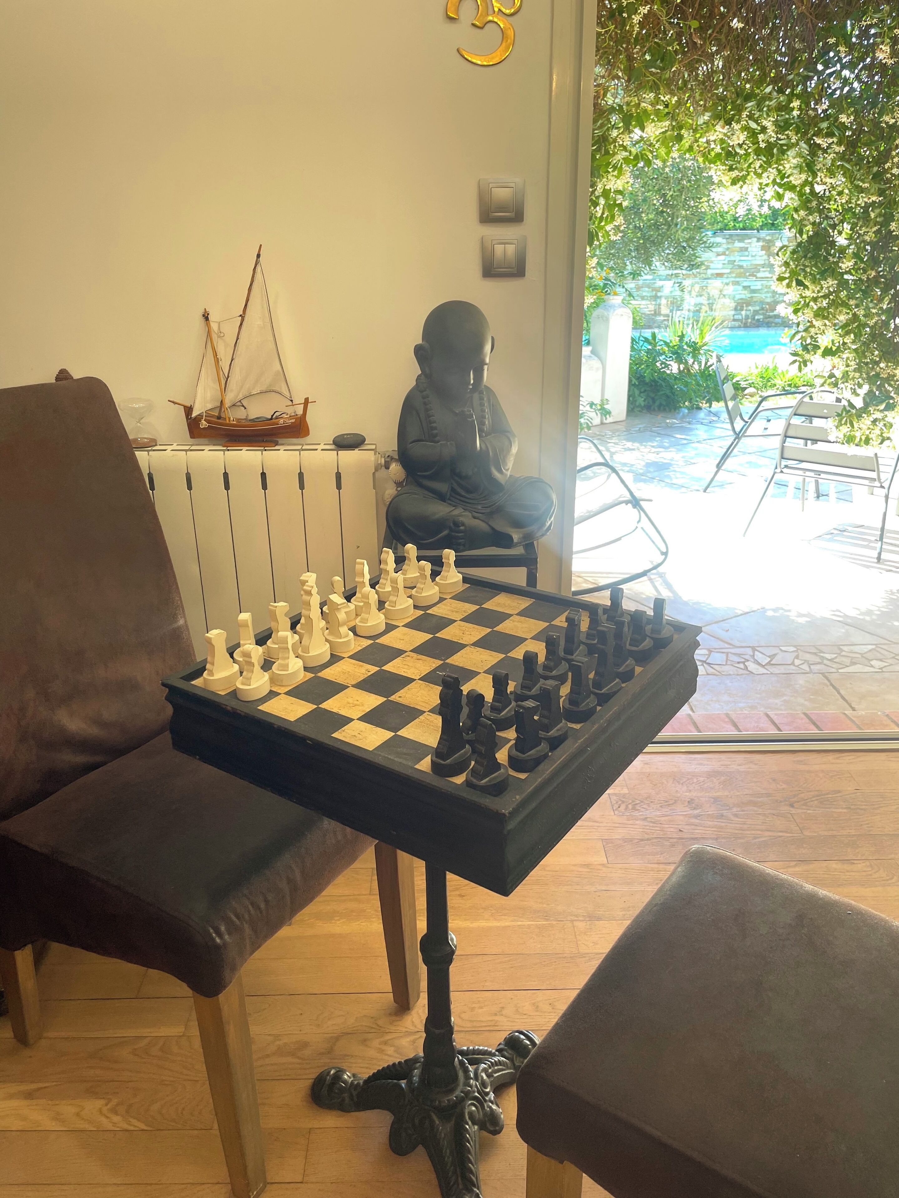 A chessboard on a table with a statue and a ship model in the background.