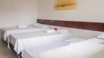 Une chambre d’hôtel avec trois lits simples, chacun doté de draps et d’oreillers blancs, et d’une tête de lit en bois.