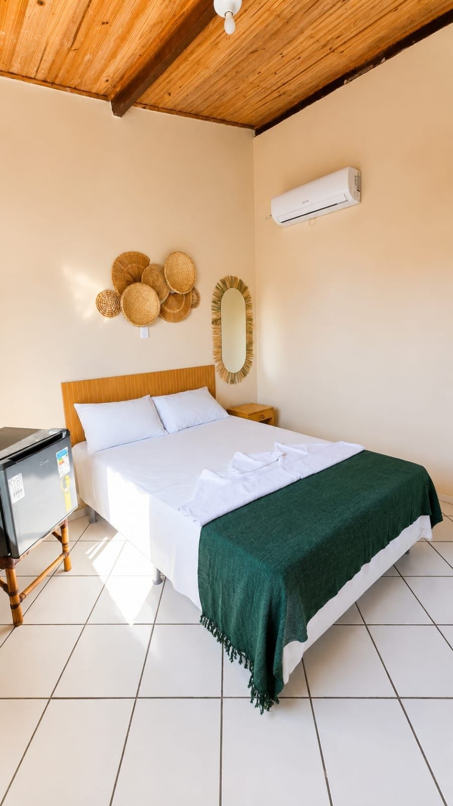 A hotel room with a bed, a wooden nightstand, a wall-mounted air conditioner, and a ceiling fan.
