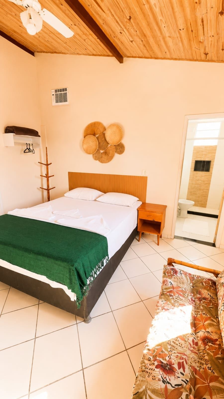 A bedroom with a bed, a nightstand, a wooden ceiling fan, a wall-mounted air conditioner, and a mirror.
