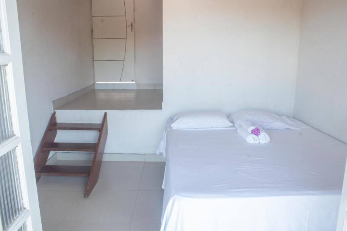 A small, clean room with a bed, a wooden ladder, and a door leading to a bathroom.