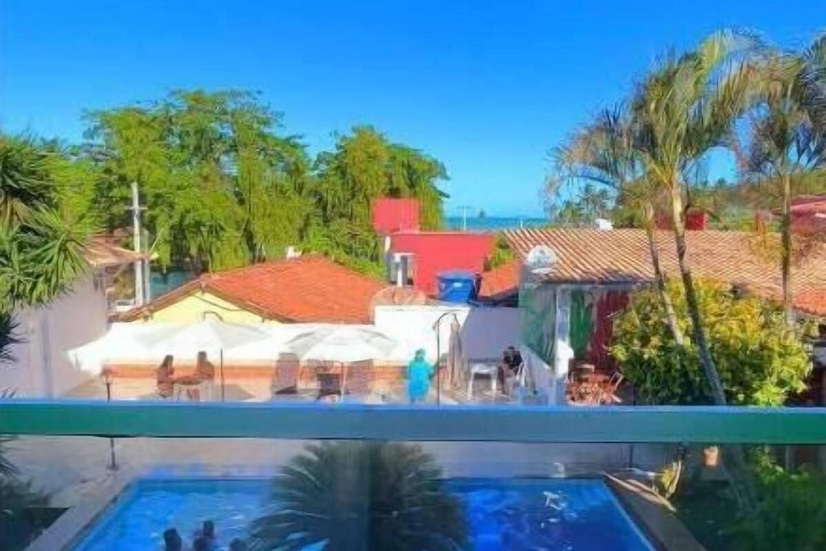 A swimming pool with people in it, surrounded by greenery and buildings with red roofs.