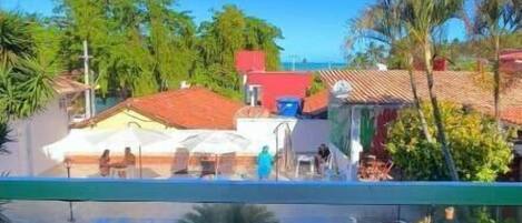 A swimming pool with people in it, surrounded by greenery and buildings with red roofs.