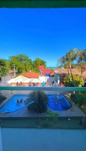 A swimming pool with people in it, surrounded by greenery and buildings with red roofs. - Pousada Terra Nostra (Prado)