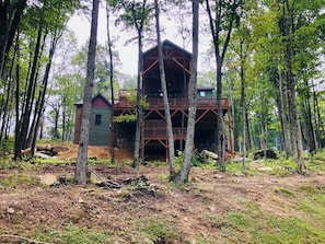 A cabin with a wooden deck and a large window, surrounded by tall trees. - Beagles Rest at Eagles Nest (Banner Elk)