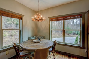 A dining area with a round table, four chairs, a chandelier, and large windows with blinds. - Adventure Hideaway at Eagles Nest (Banner Elk)