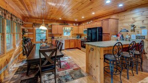 A wooden cabin interior with a dining area, kitchen, and bar seating. - Carolina Charm (Banner Elk)