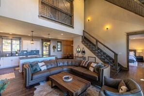 A spacious living area with a large L-shaped sectional sofa, a wooden coffee table, and a staircase leading to an upper level. - Birds Eye View at Eagles Nest (Banner Elk)