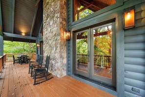 A covered deck with outdoor furniture and a stone wall. - Highlander Hideaway (Newland)