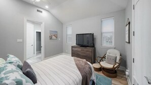 A bedroom with a bed, a dresser, a television, a chair, and a ceiling fan.