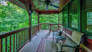 A covered porch with a ceiling fan, wooden railings, and a view of a forest. - Uncle Johns Cabin (Vilas)