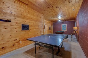 Una mesa de ping pong en una habitación con paredes de madera y una mesa de billar.